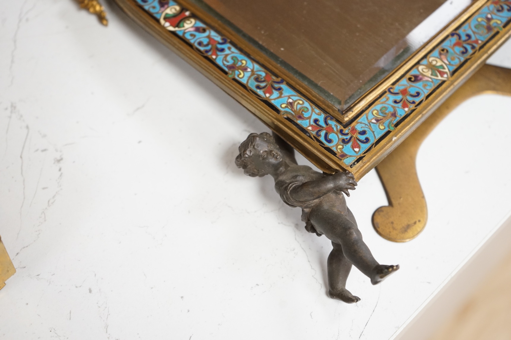 A champleve enamel easel mirror with putti supports, 28cm high.